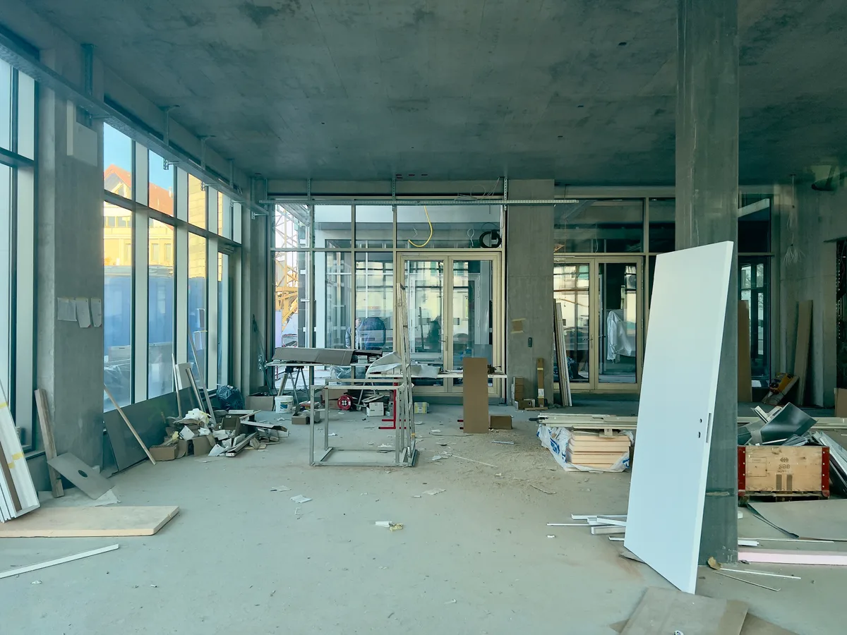 Man sieht durch ein Fenster in einen Rohbau. Überall liegt Baumaterial verstreut.